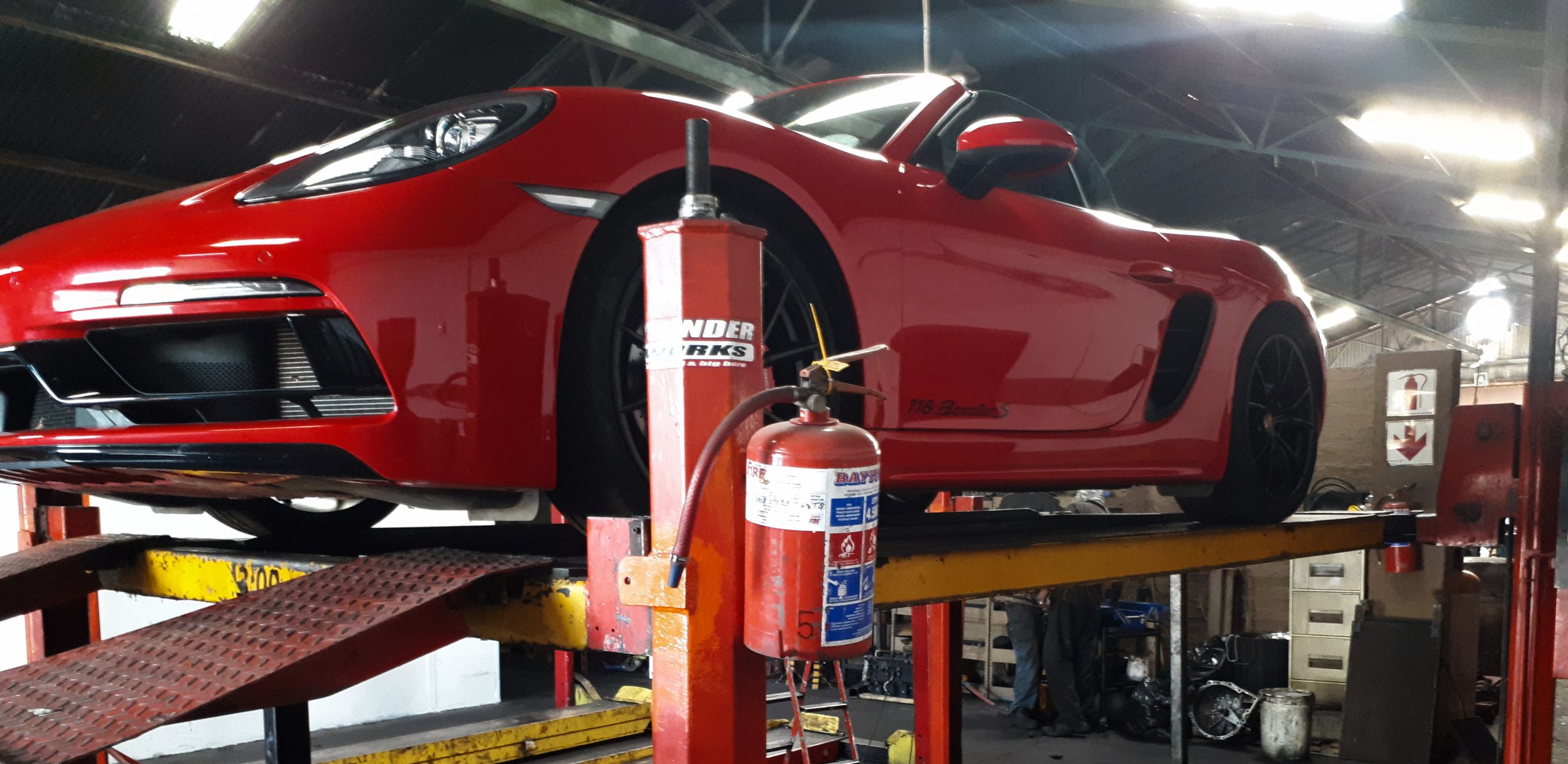 MECHANICAL 1 red sports car on a hydraulic lift being repaired by the xxx exhaust team