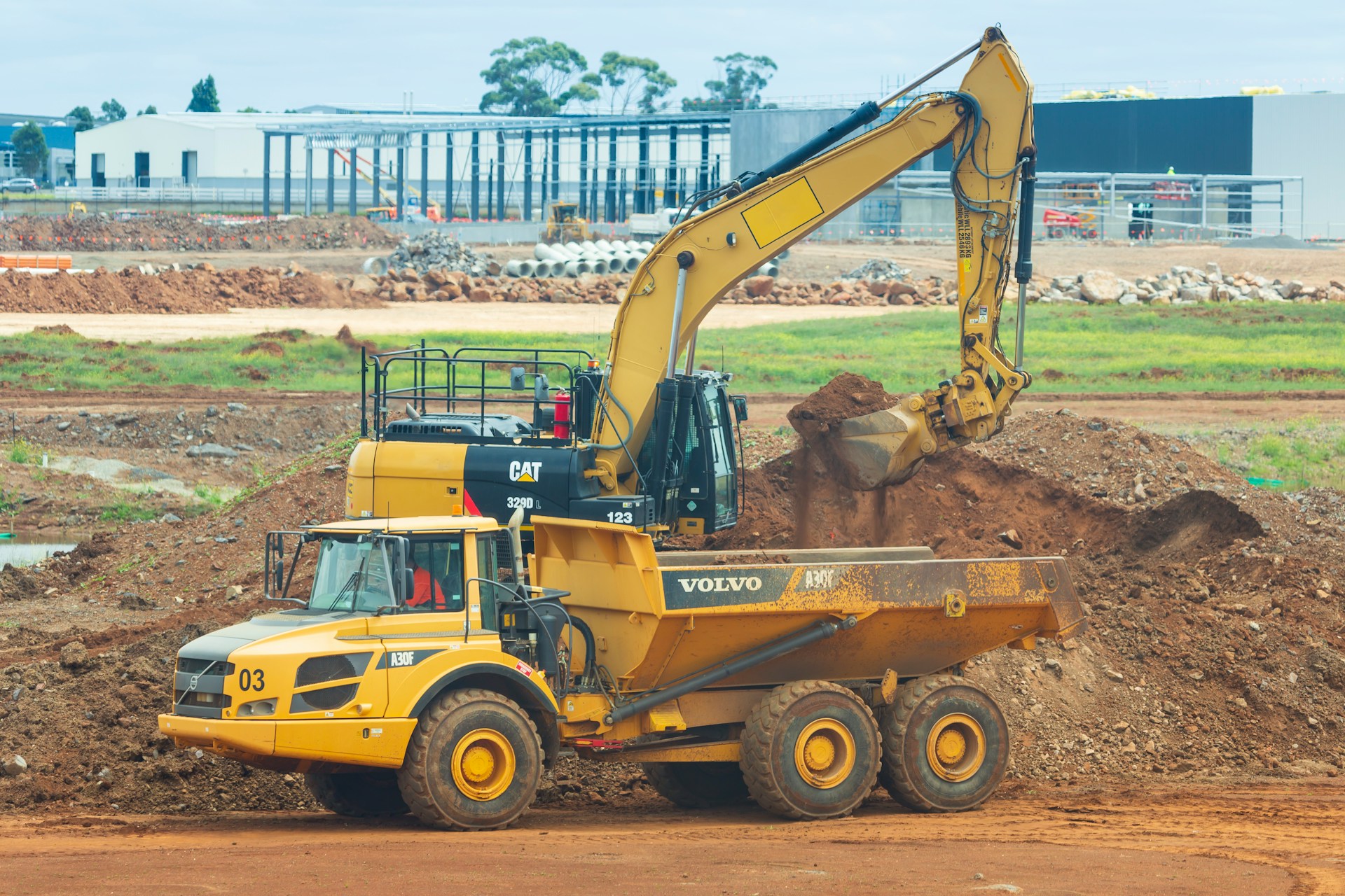 Earthmoving machinery in the foreground with factories being built in the distance